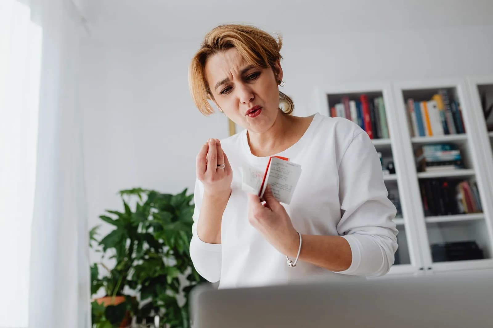 Mulher com expressão preocupada segurando um recibo em casa