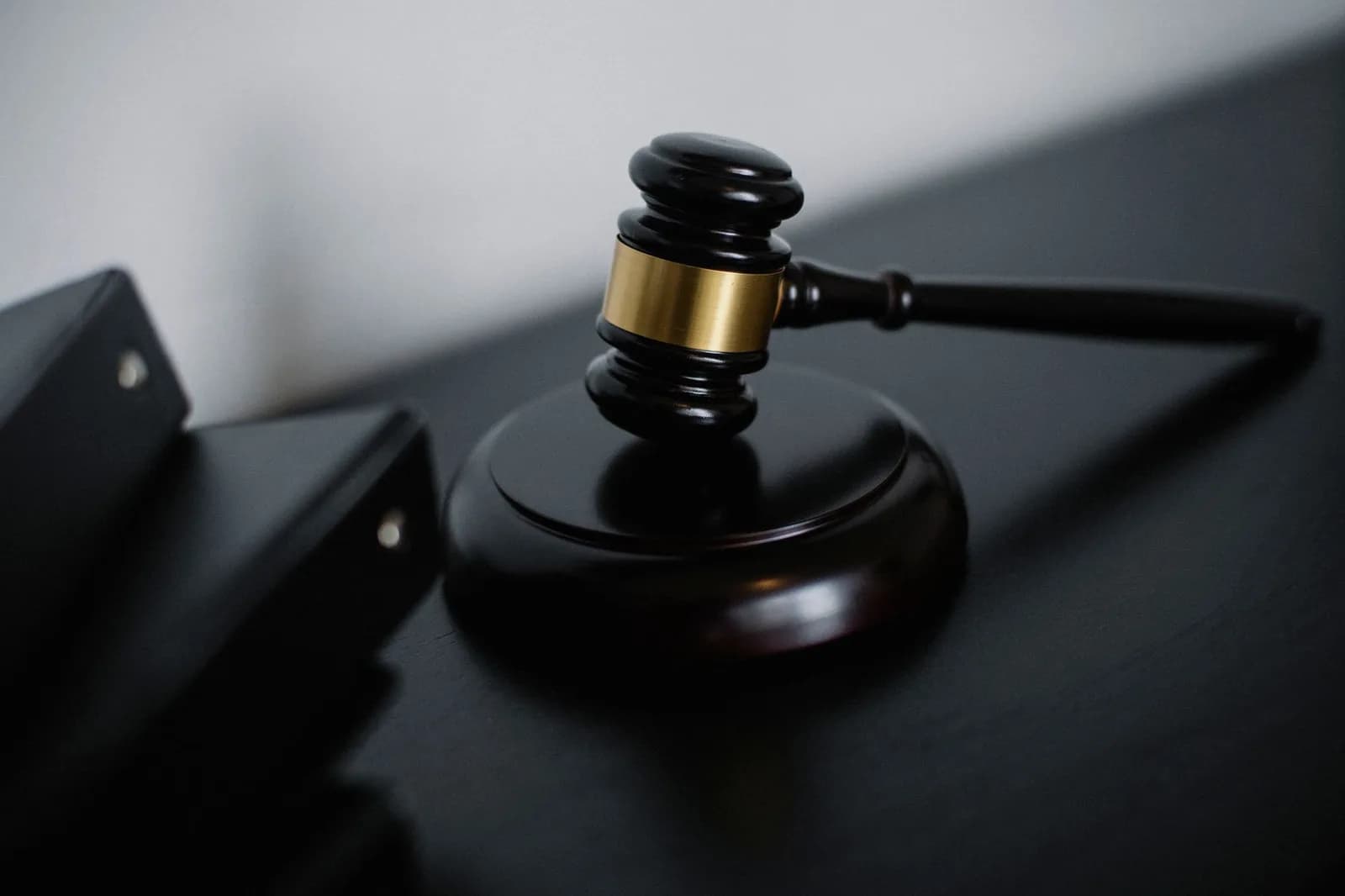 Martelo de madeira da Justiça apoiado sobre mesa escura ao lado de pastas processuais