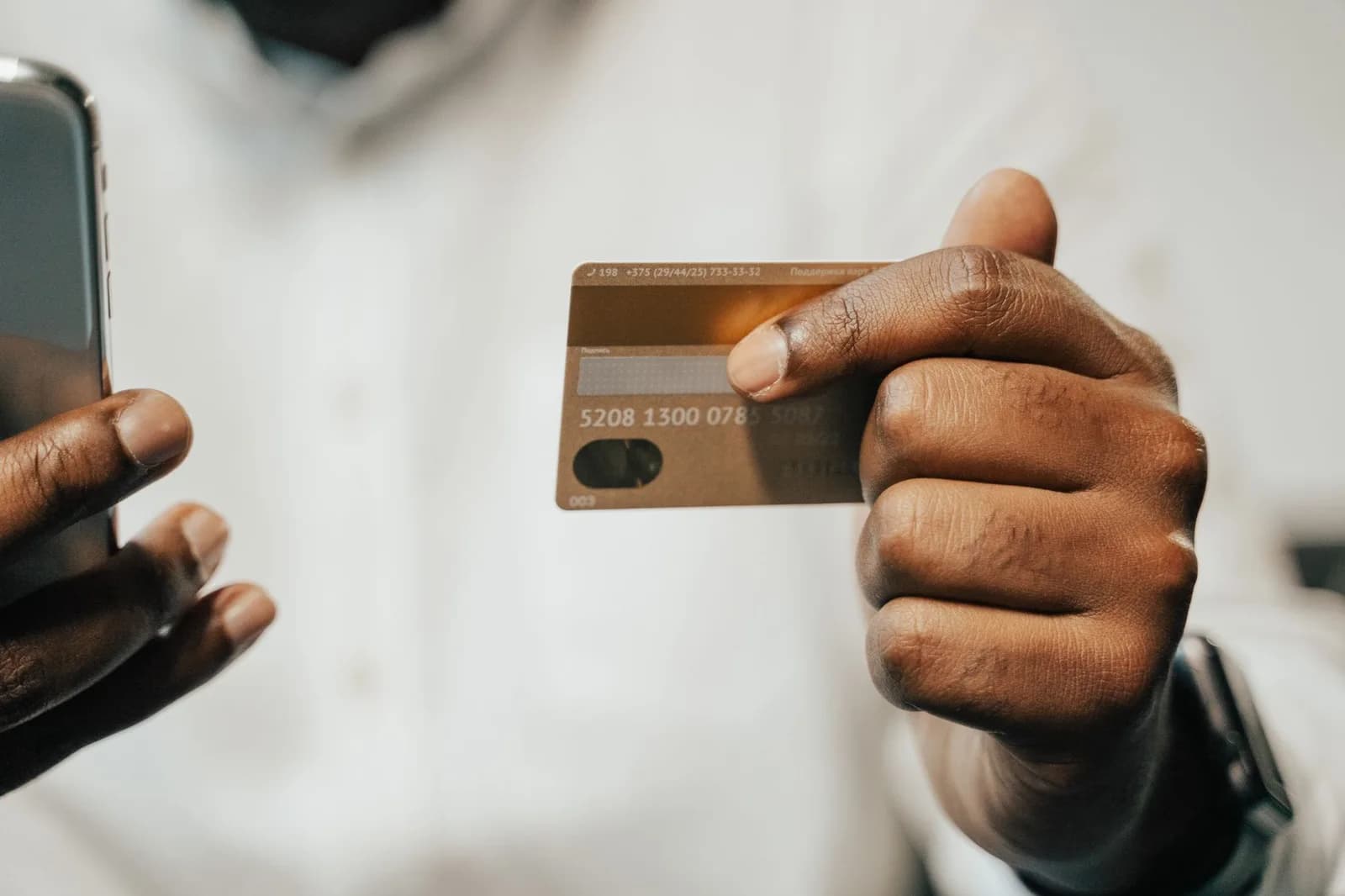 Mão segurando cartão bancário e celular, em ambiente claro
