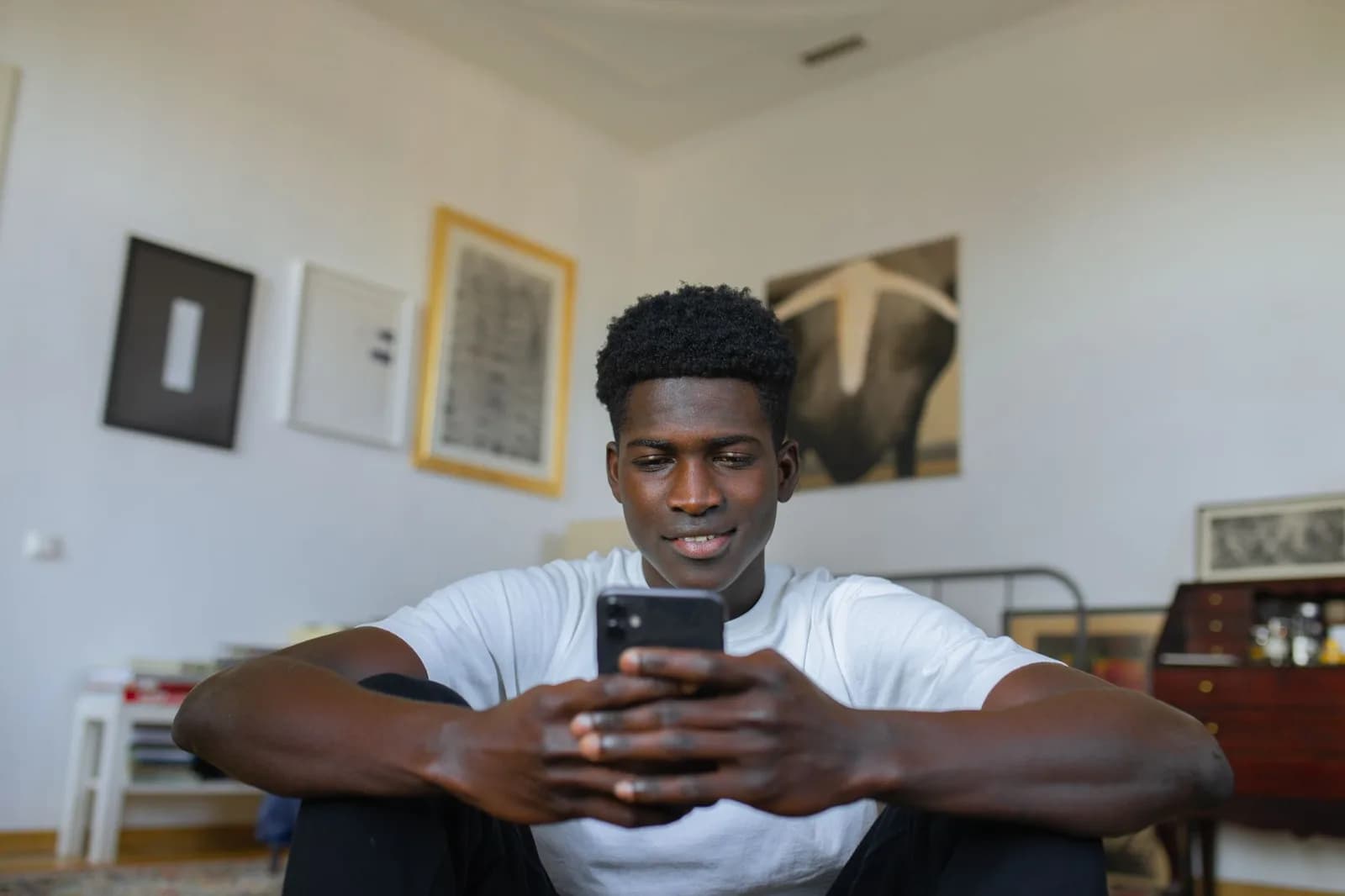 Jovem sentado no chão da sala usa o celular