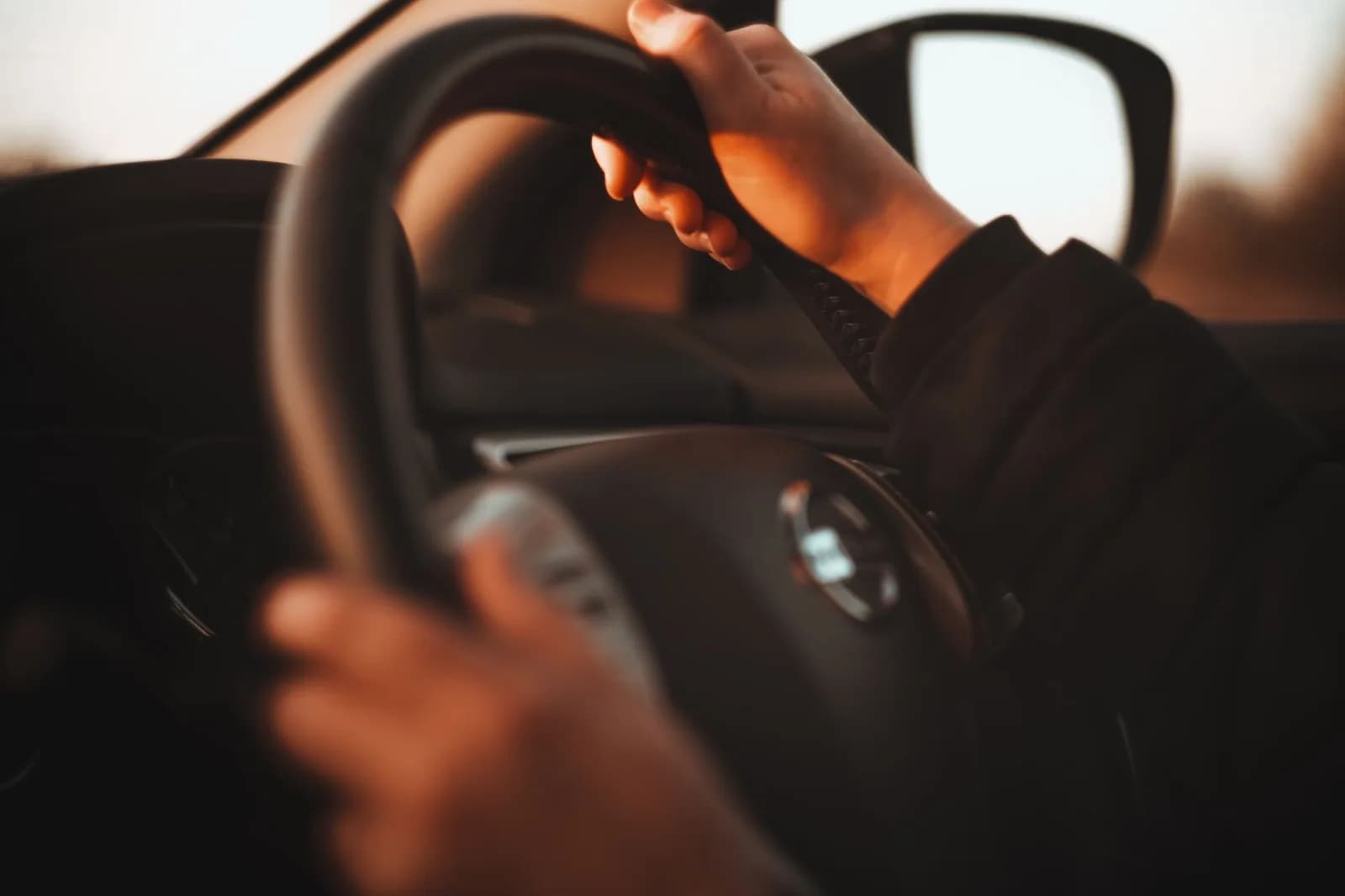 Mãos no volante de um carro, em cena de direção ao entardecer