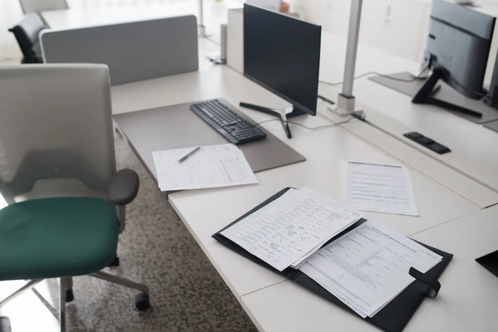 Mesa de escritório com pasta e papéis abertos ao lado do computador