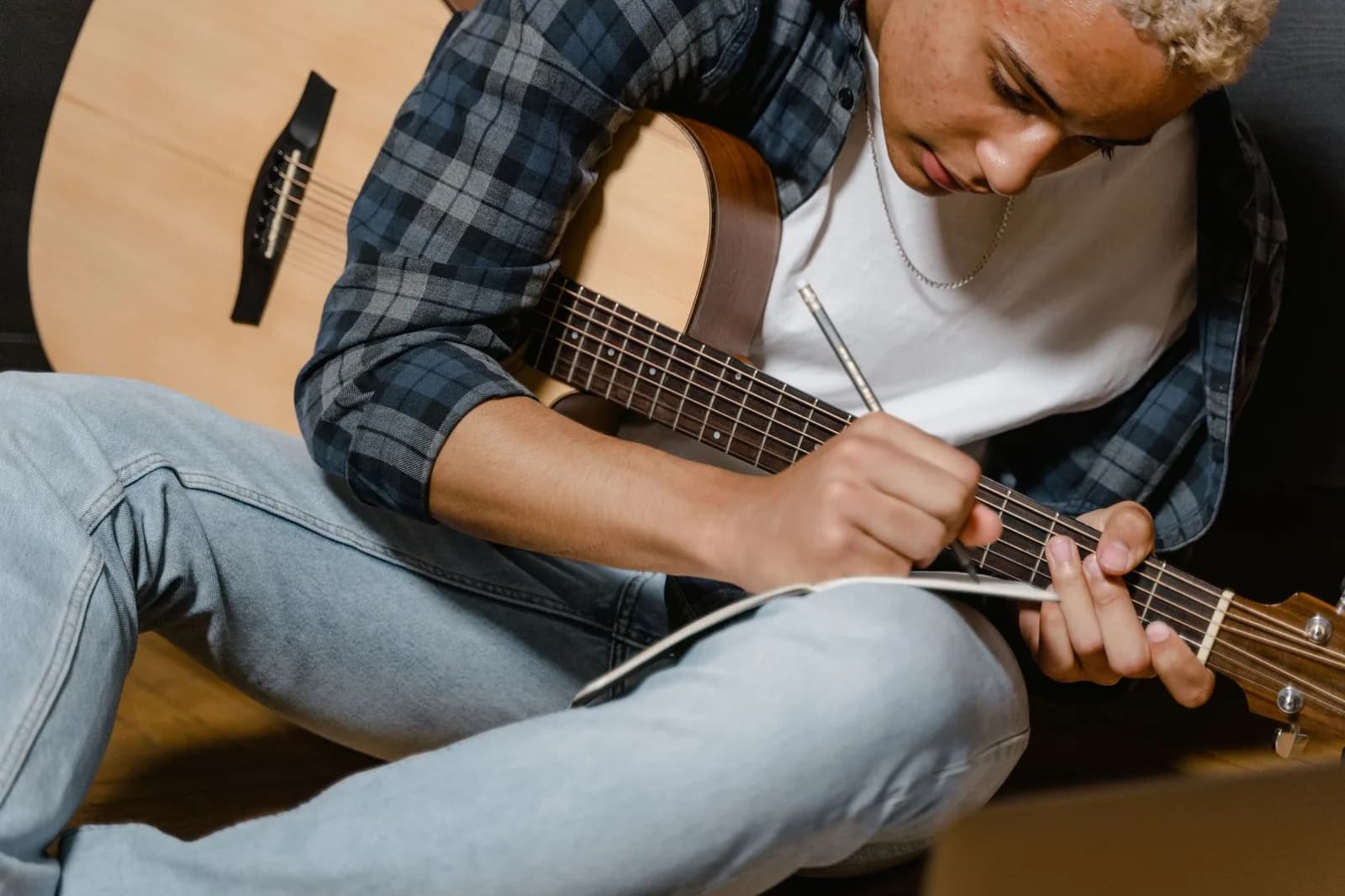 Jovem com violão escreve letras de música em um caderno