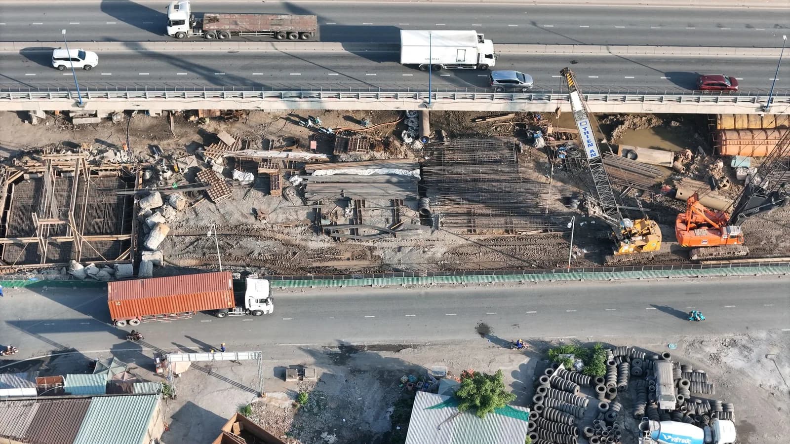 Vista aérea de obra de recuperação em ponte de rodovia com maquinário e caminhões ao lado