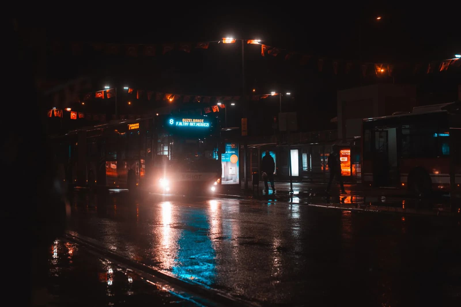 Terminal de ônibus à noite, com veículos e piso molhado