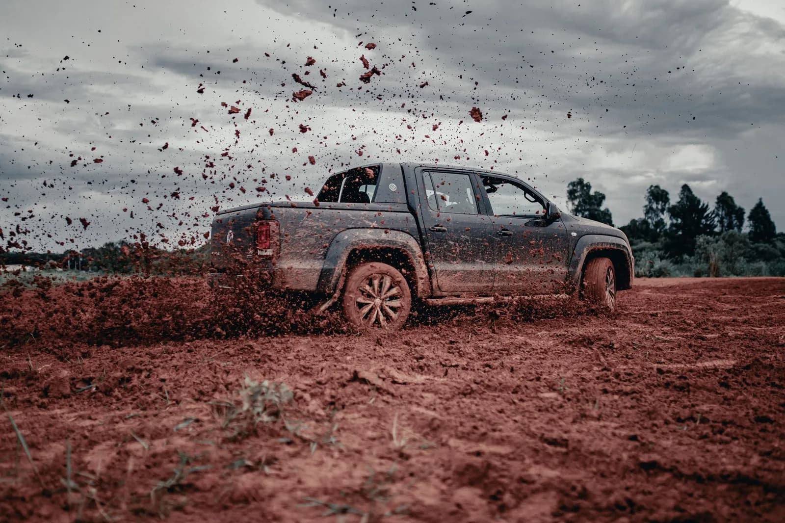 Caminhonete cabine dupla acelerando em estrada de terra vermelha, levantando terra em percurso off-road