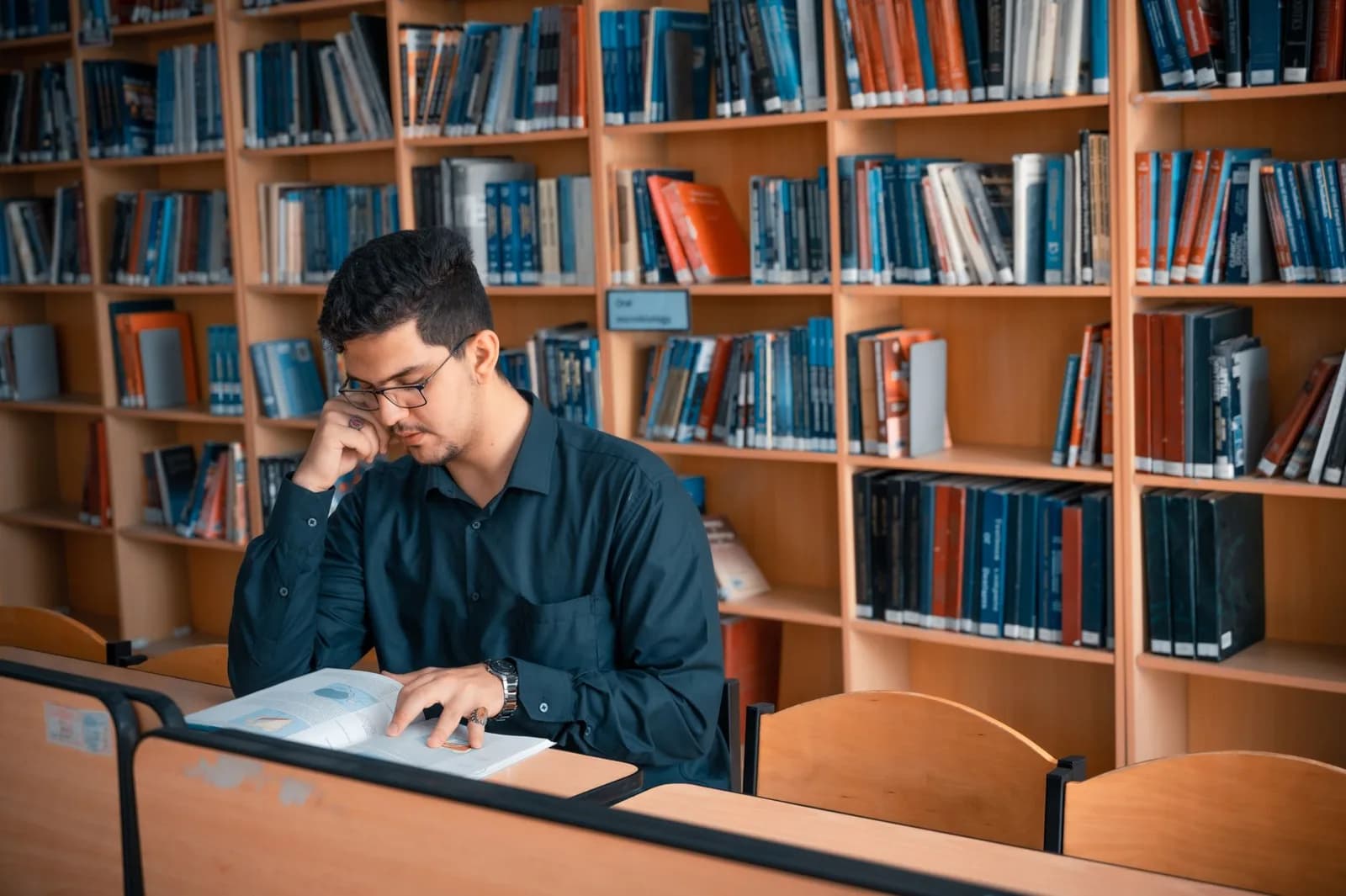 Estudante lendo livro em mesa de estudos em biblioteca universitaria