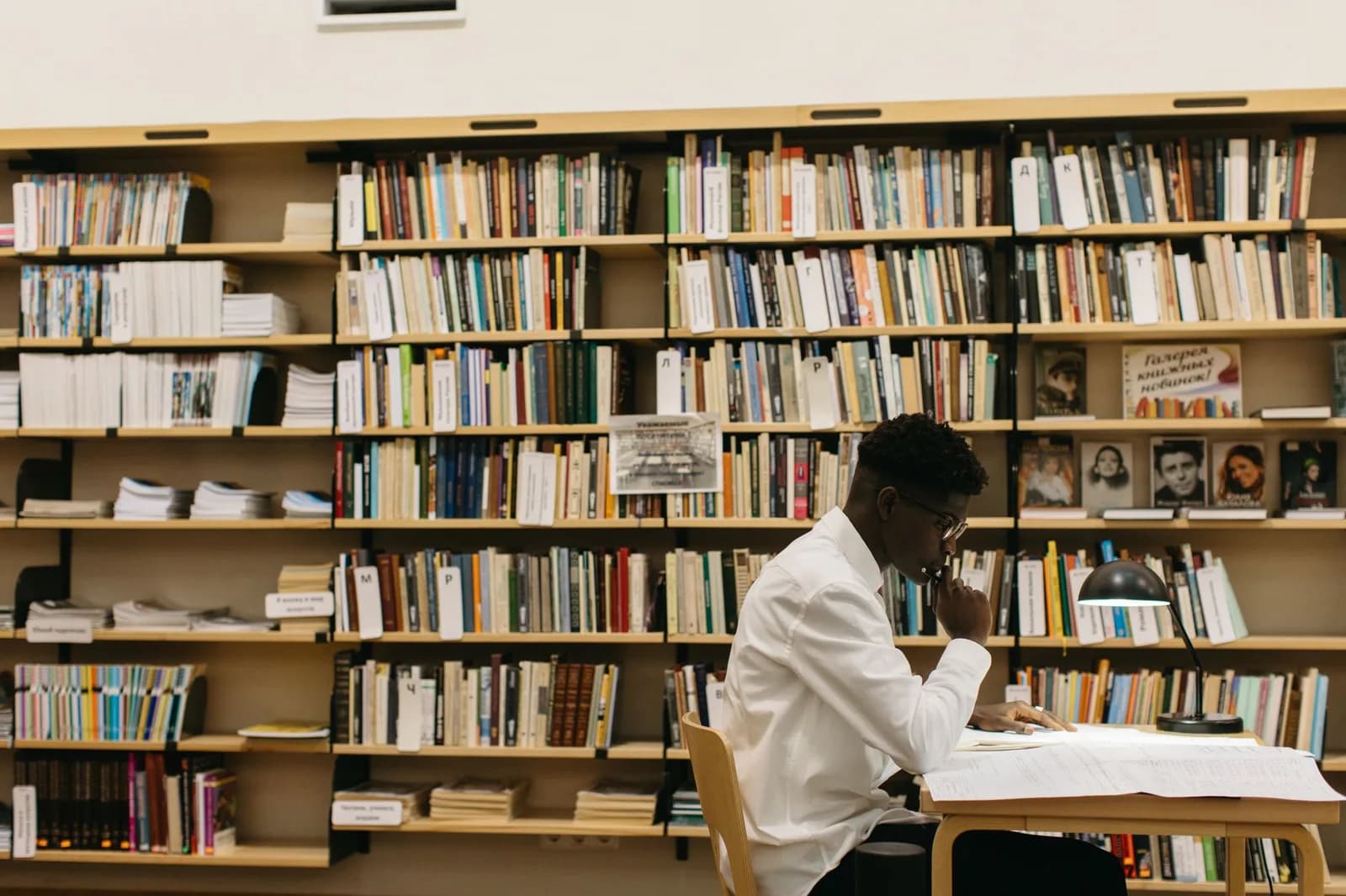 Estudante lê e faz anotações em mesa de biblioteca cercada de livros