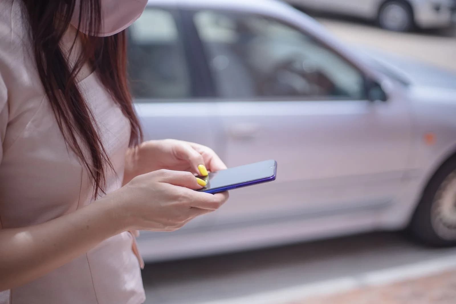 Mulher usa o celular ao lado de um carro prata