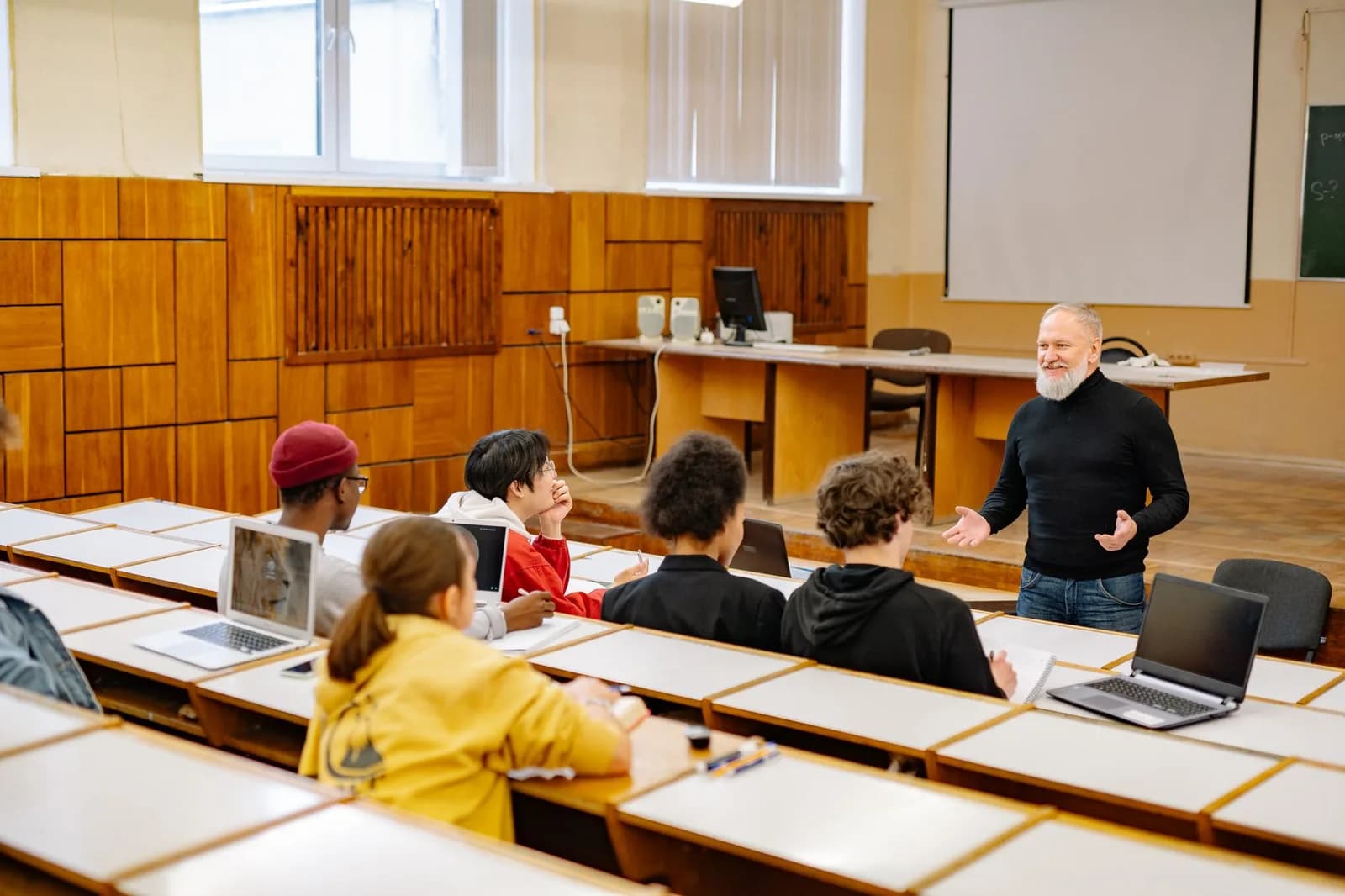 Professor conversa com alunos em sala de aula com notebooks