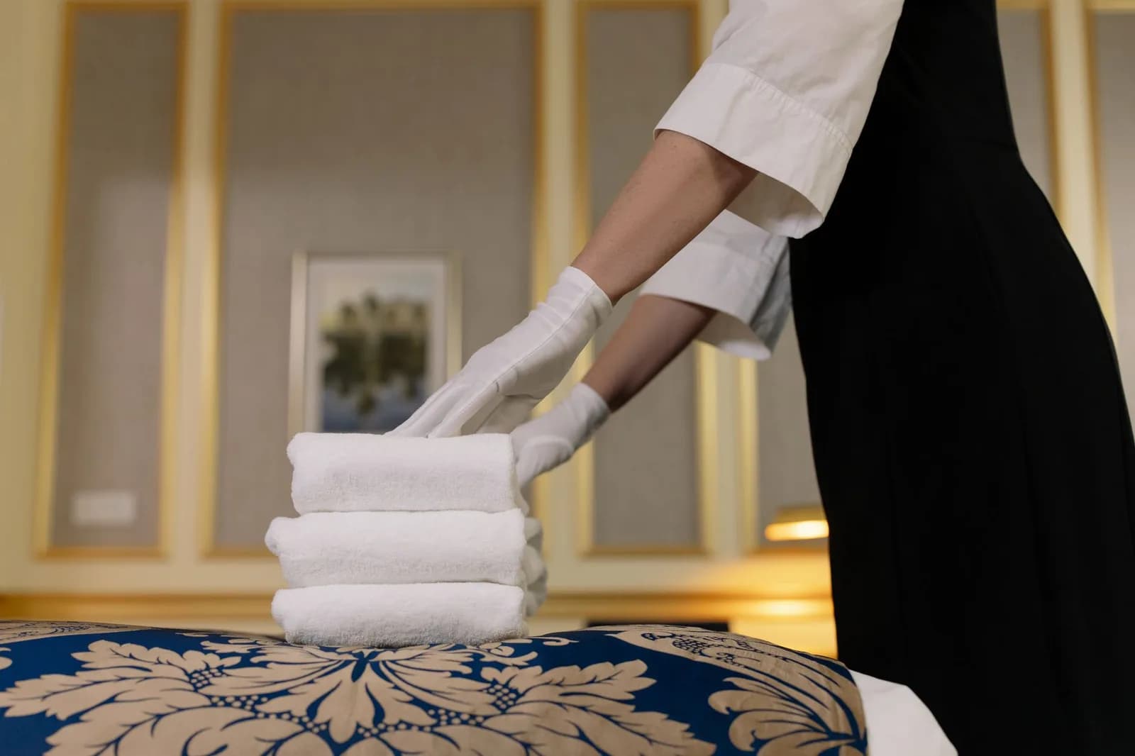 Mãos de luvas brancas dobram toalhas em quarto de hotel