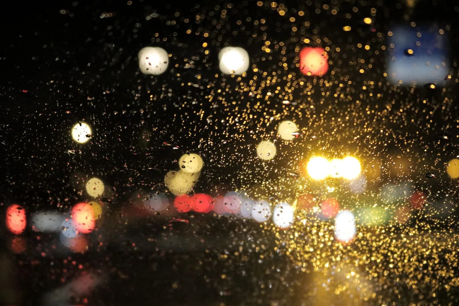 Gotas de chuva no vidro do carro, com as luzes da rua desfocadas ao fundo