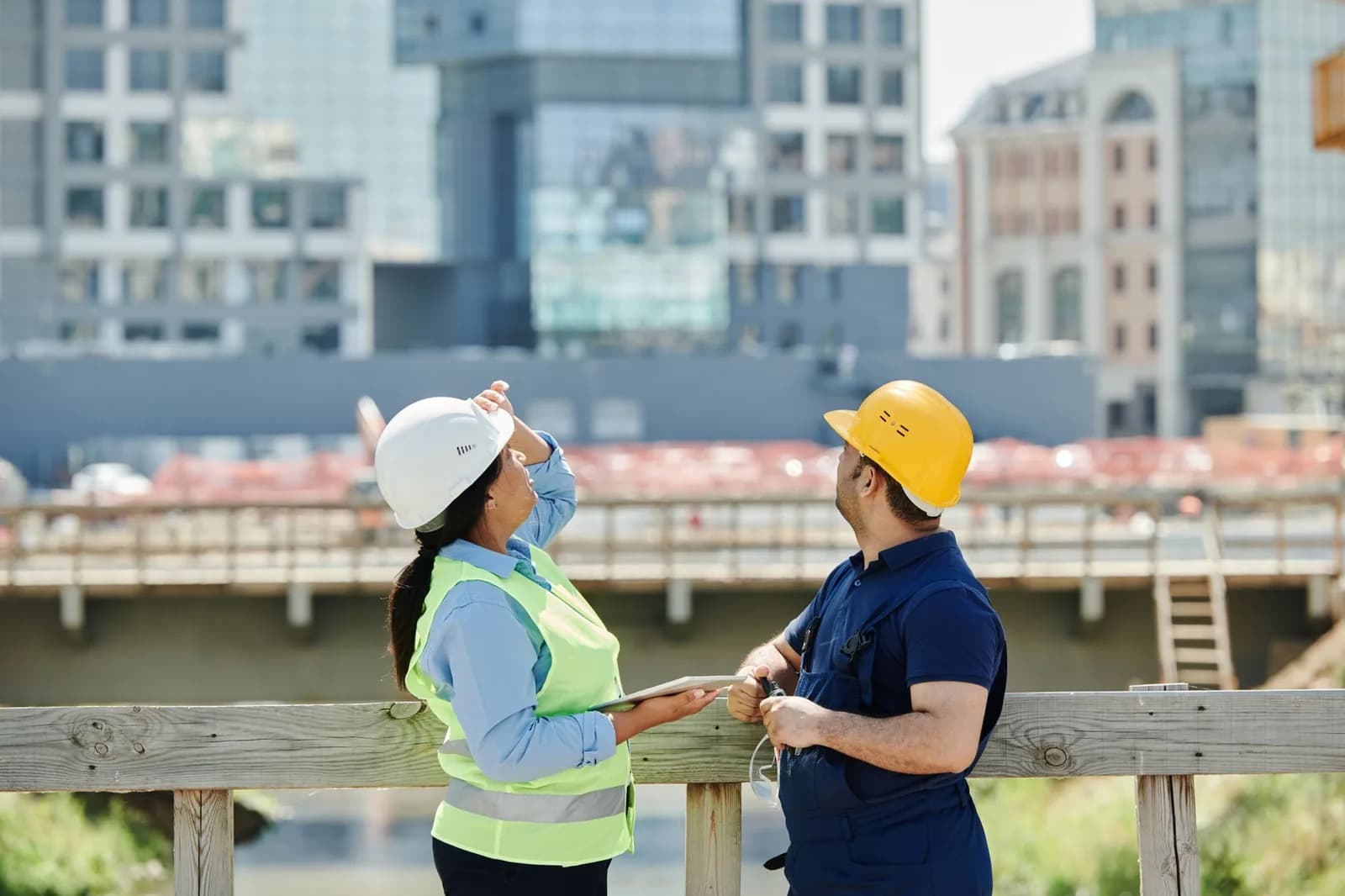 Profissionais de engenharia civil de capacete observando canteiro de obras e edificacoes urbanas