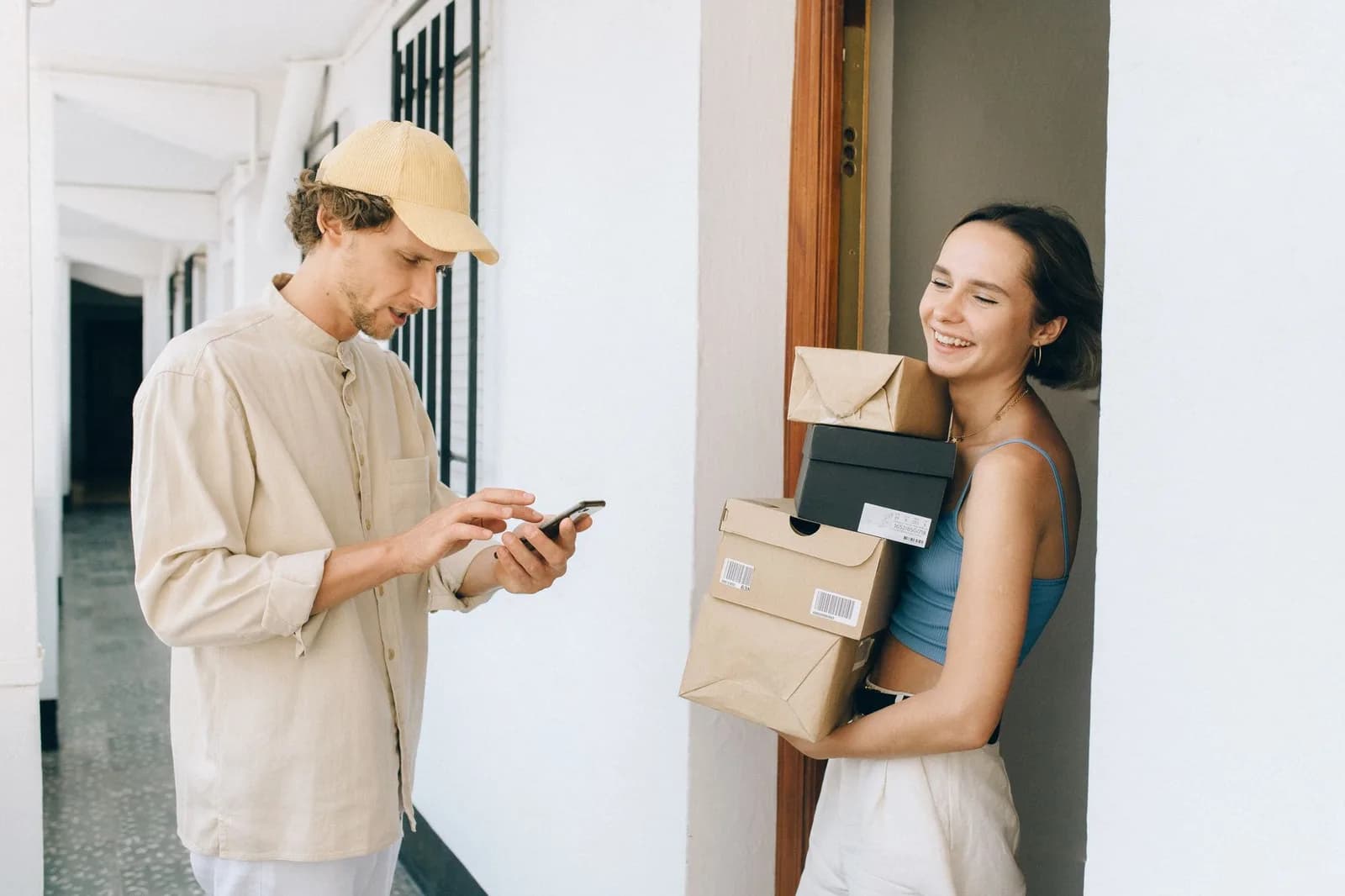 Entregador confere o celular enquanto mulher recebe encomendas na porta de casa