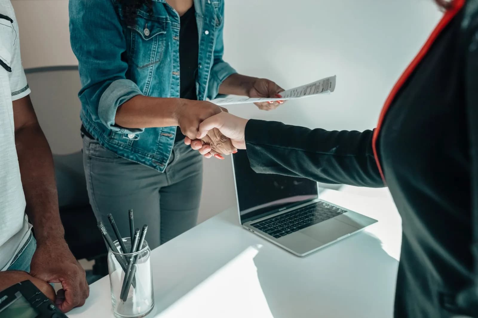 Profissionais apertando as mãos sobre mesa de escritório com documentos de acordo e computador