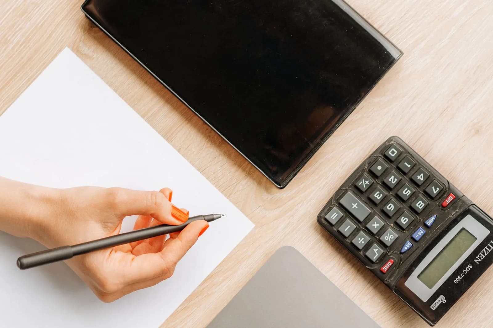 Mão escrevendo em folha de papel em branco, com calculadora ao lado