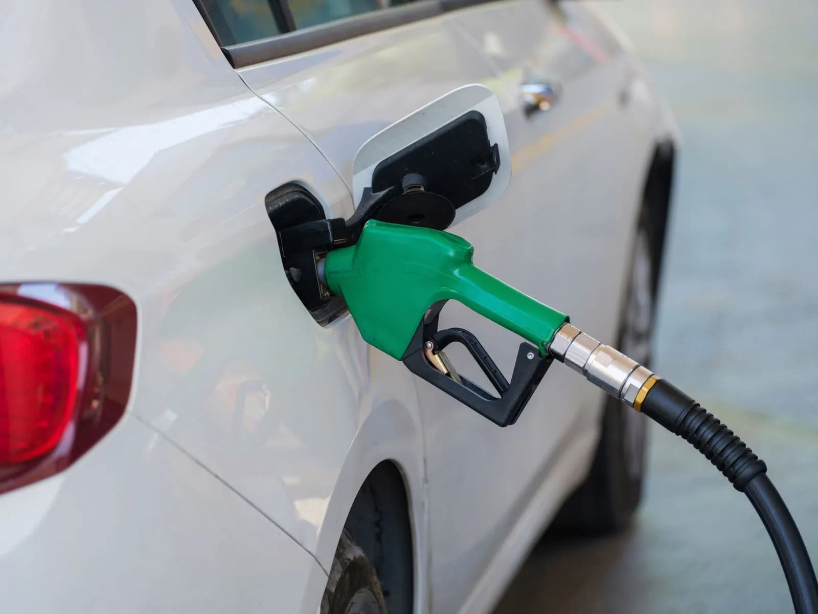 Bico de bomba verde abastecendo um carro branco em posto de gasolina