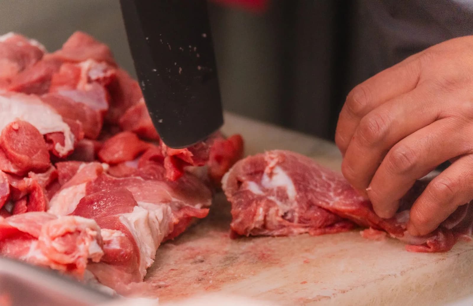 Trabalhador manipulando e cortando pecas de carne em bancada de processamento