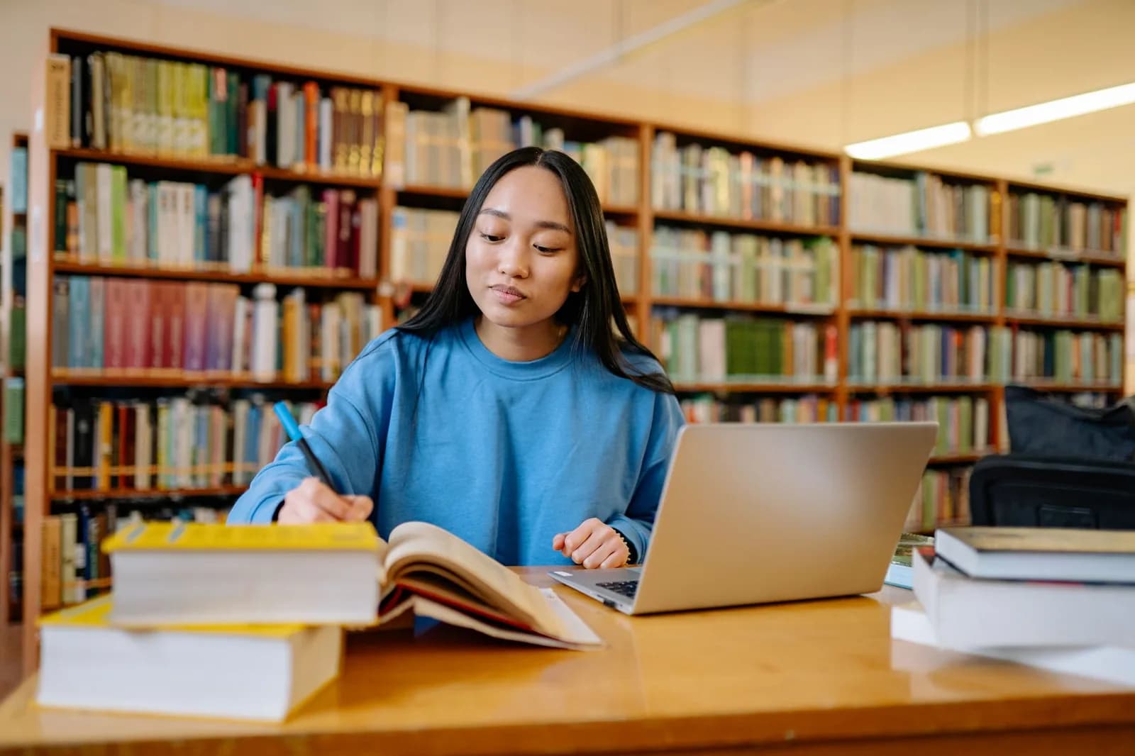 Estudante com fones de ouvido estuda com laptop cercada de livros em biblioteca