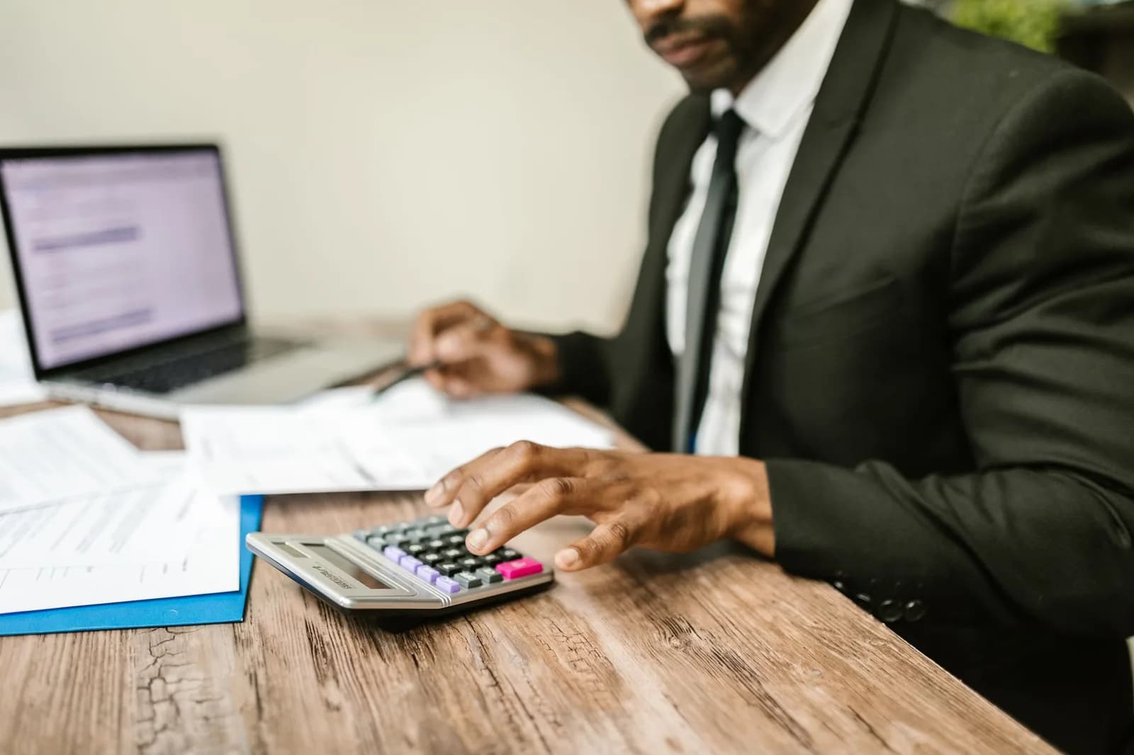 Profissional de terno analisando contas e utilizando calculadora em mesa de escritório com documentos