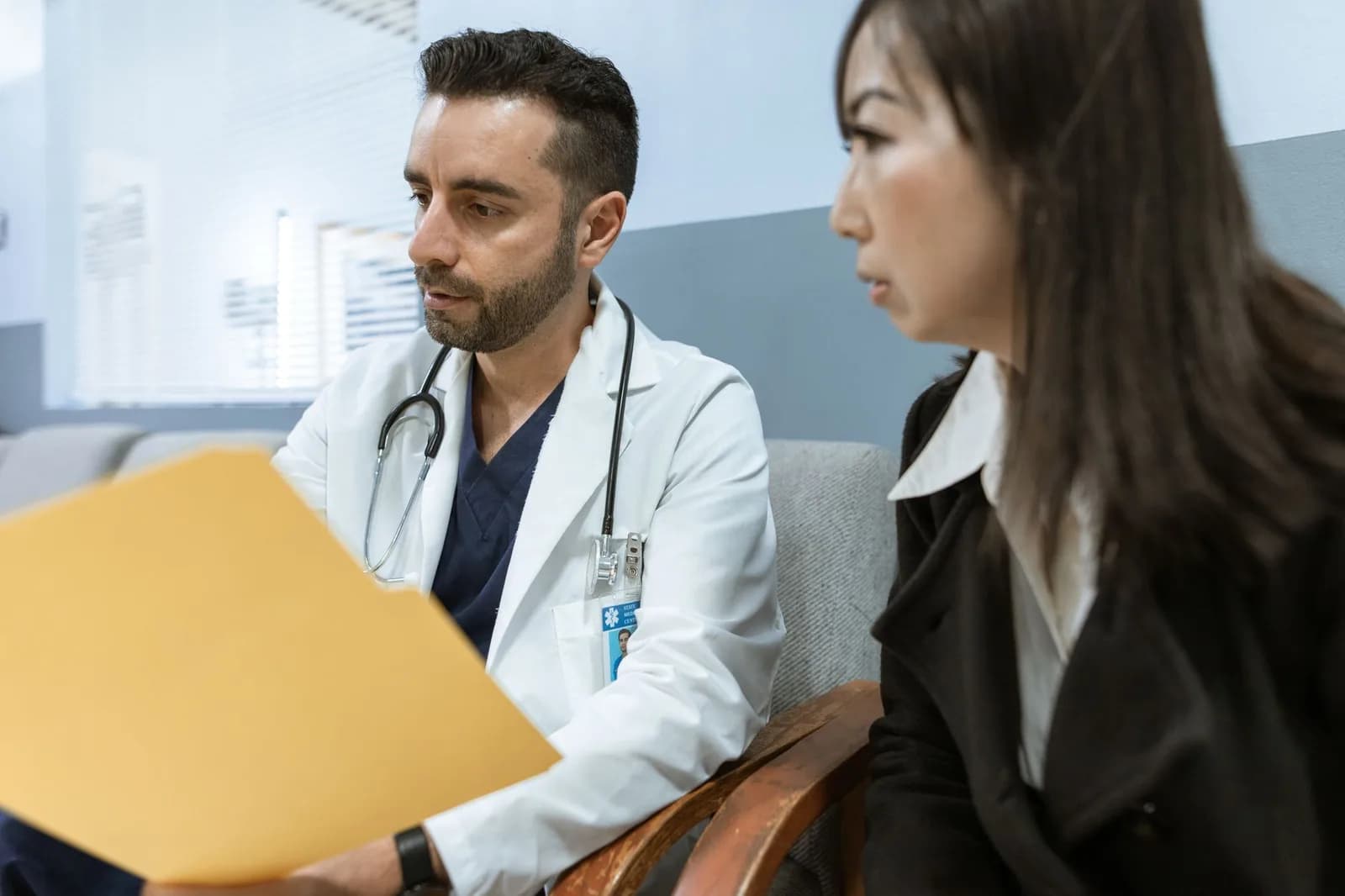 Médico consulta paciente em consultório, com pasta de documentos em mãos