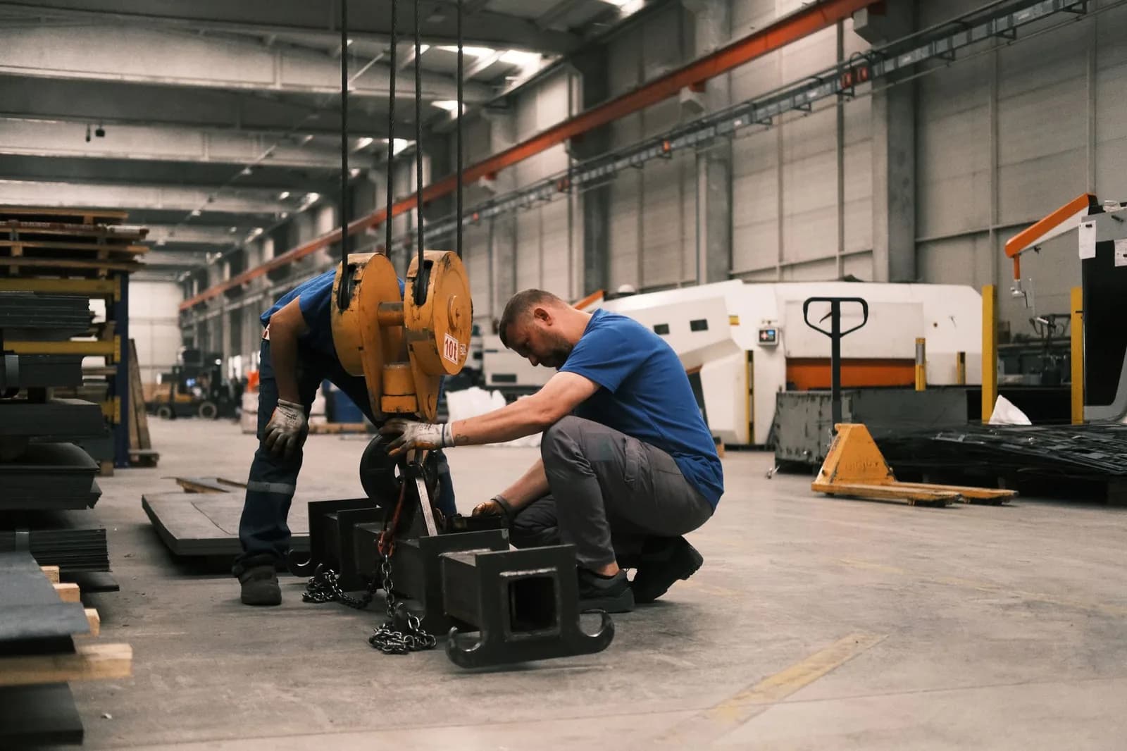 Dois trabalhadores ajustam equipamento pesado em galpão industrial