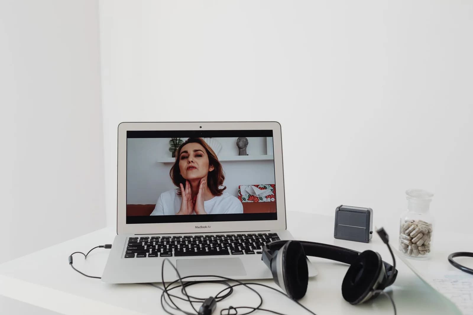 Profissional de saúde em consulta por videochamada, com notebook e fones sobre a mesa