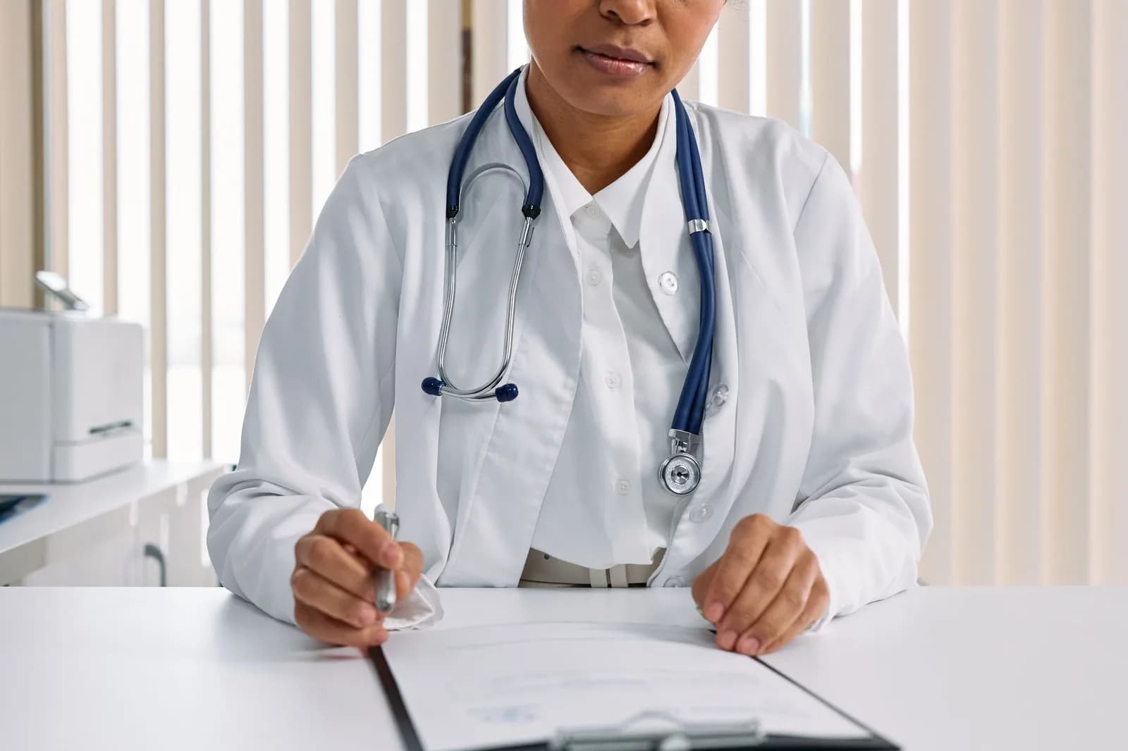 Médica de jaleco branco com estetoscópio sobre a mesa em consulta de saúde