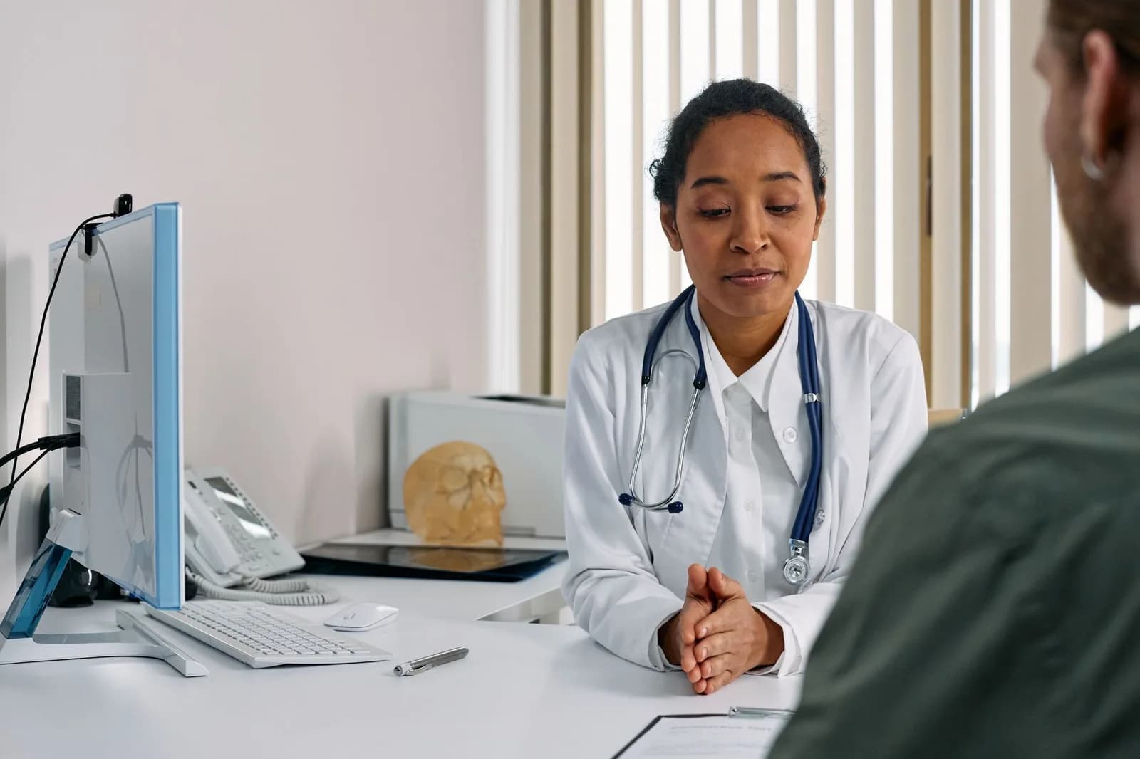 Médica de jaleco conversa com paciente em consultório