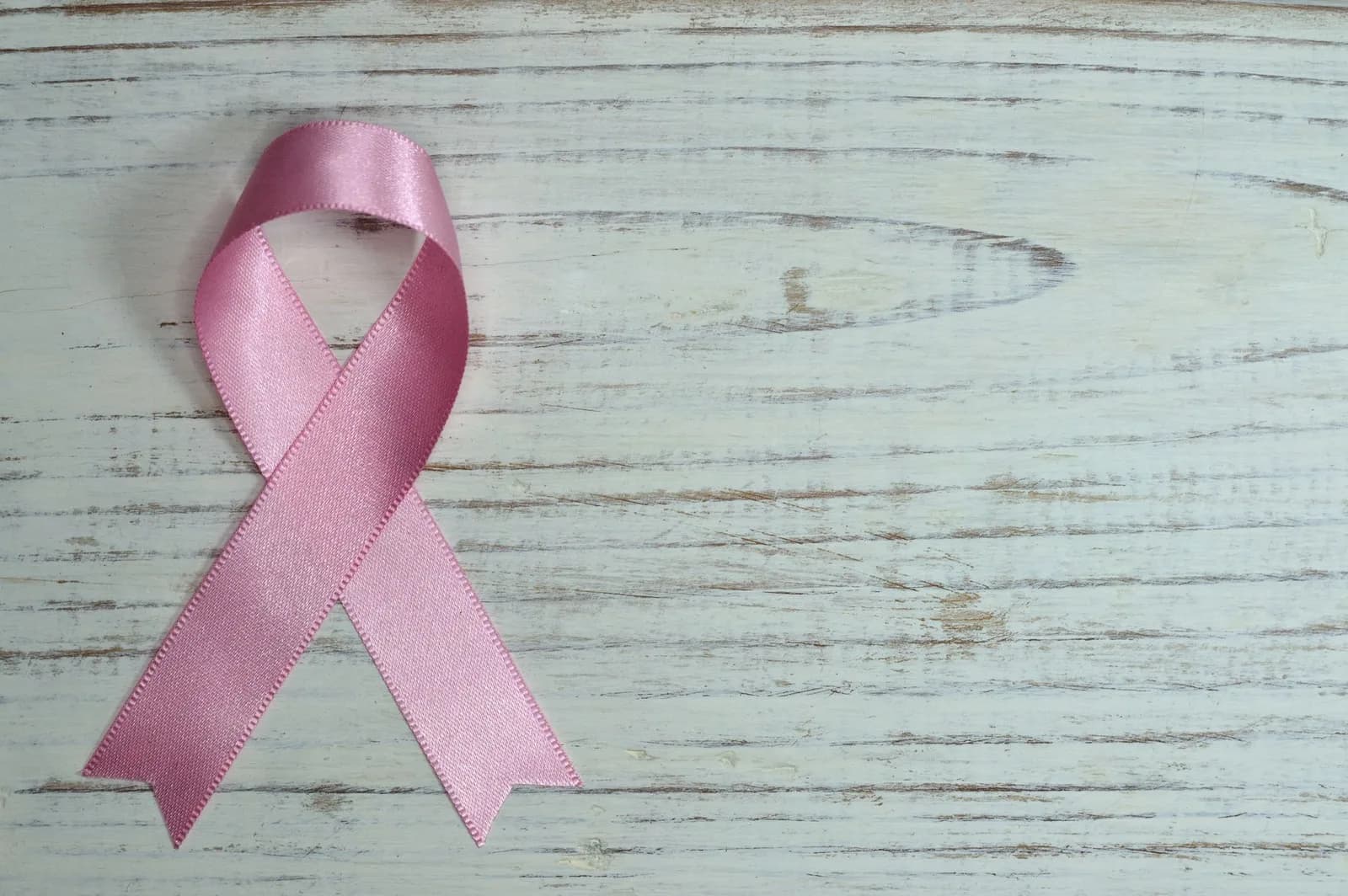 Laço rosa da campanha Outubro Rosa sobre superfície de madeira clara.