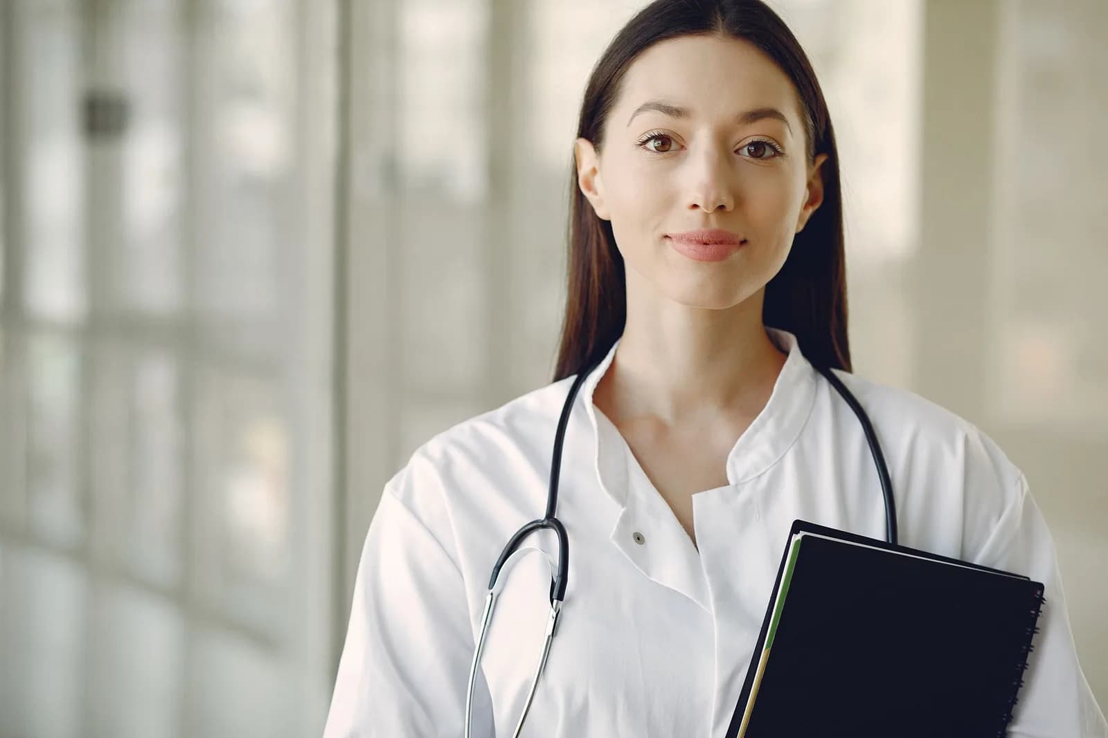 Médica com estetoscópio e pasta sorrindo para câmera
