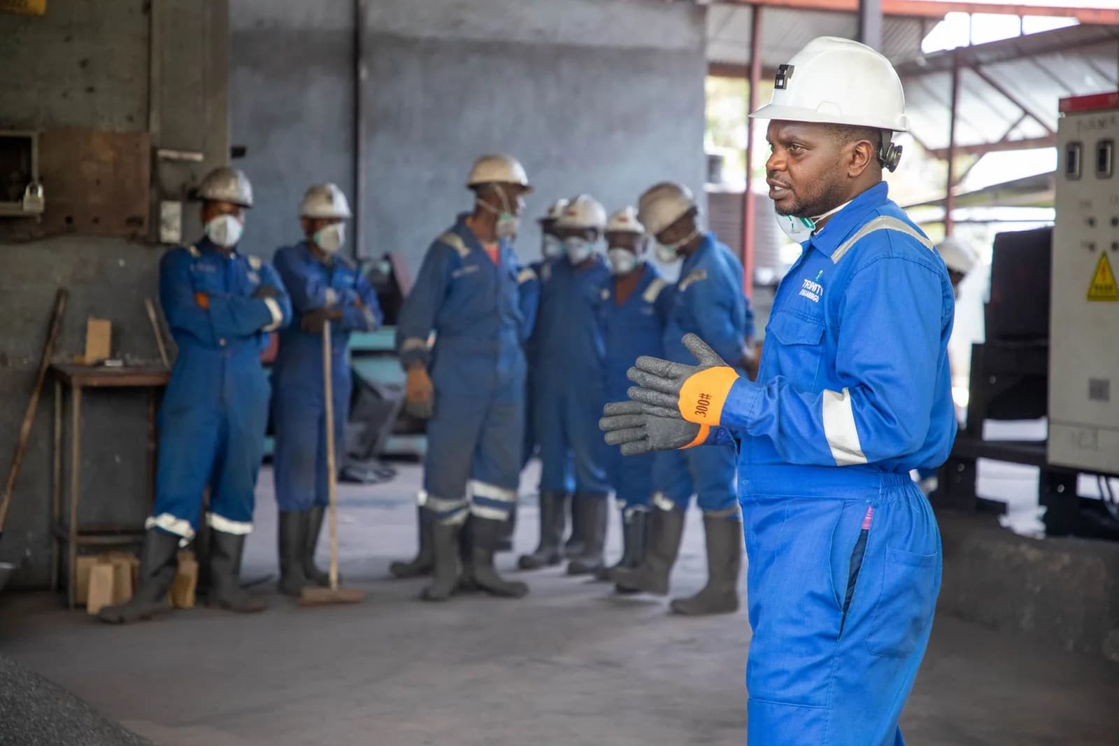 Trabalhadores de macacão azul e capacete ouvem orientação em fábrica