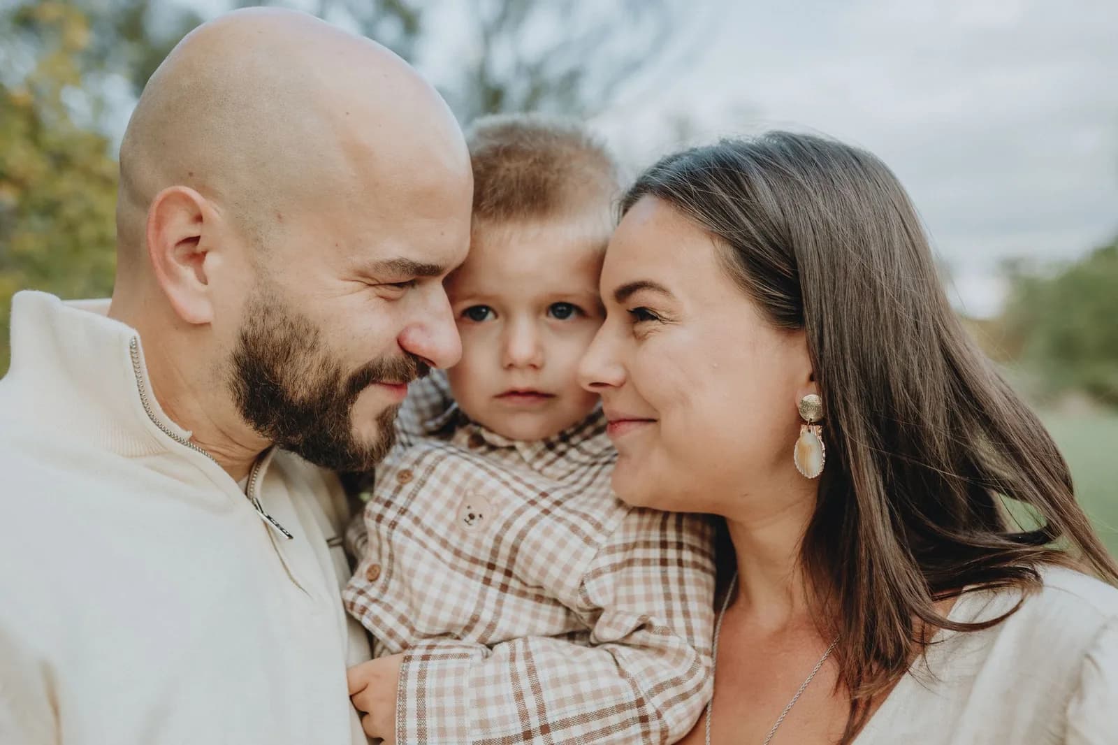 Casal com uma criança de colo em abraço familiar ao ar livre.