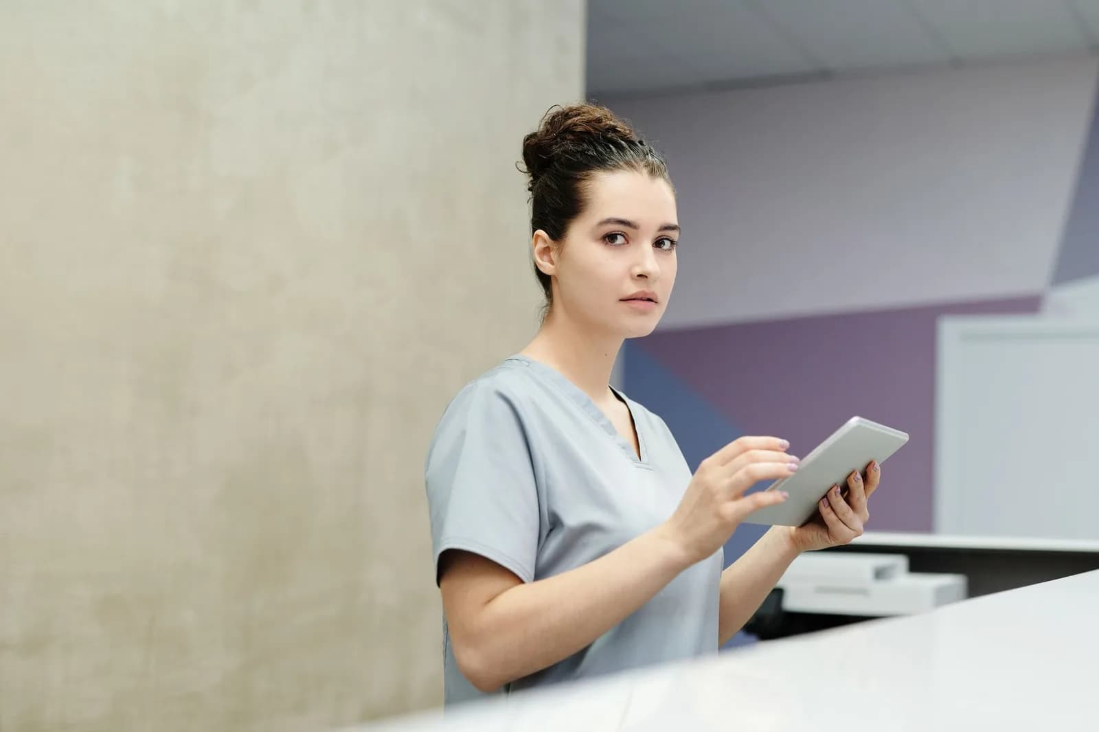 Profissional de saúde de uniforme com tablet na recepção de um hospital.