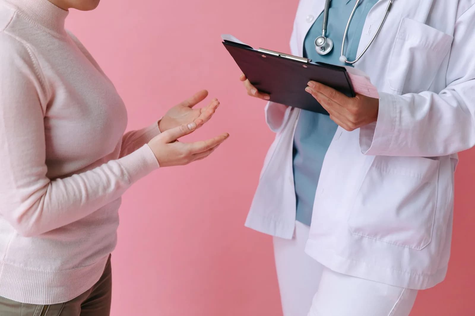 Médica com prancheta conversa com paciente em fundo rosa