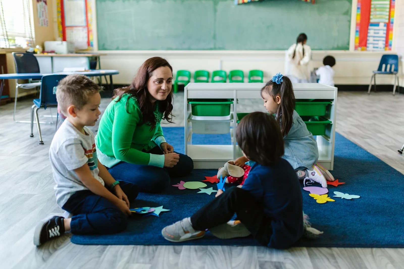 Professora sentada no chão com crianças em sala de educação infantil.